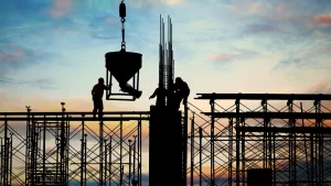 Trabalhadores da construção civil em atividade sobre estrutura de concreto com vergalhões aparentes, avaliando a escolha entre estrutura metálica ou concreto.
