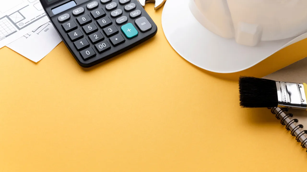 Mesa de planejamento com calculadora, capacete de segurança branco, pincel, prancheta e planta baixa, simbolizando estratégias para redução de custos em obras industriais.