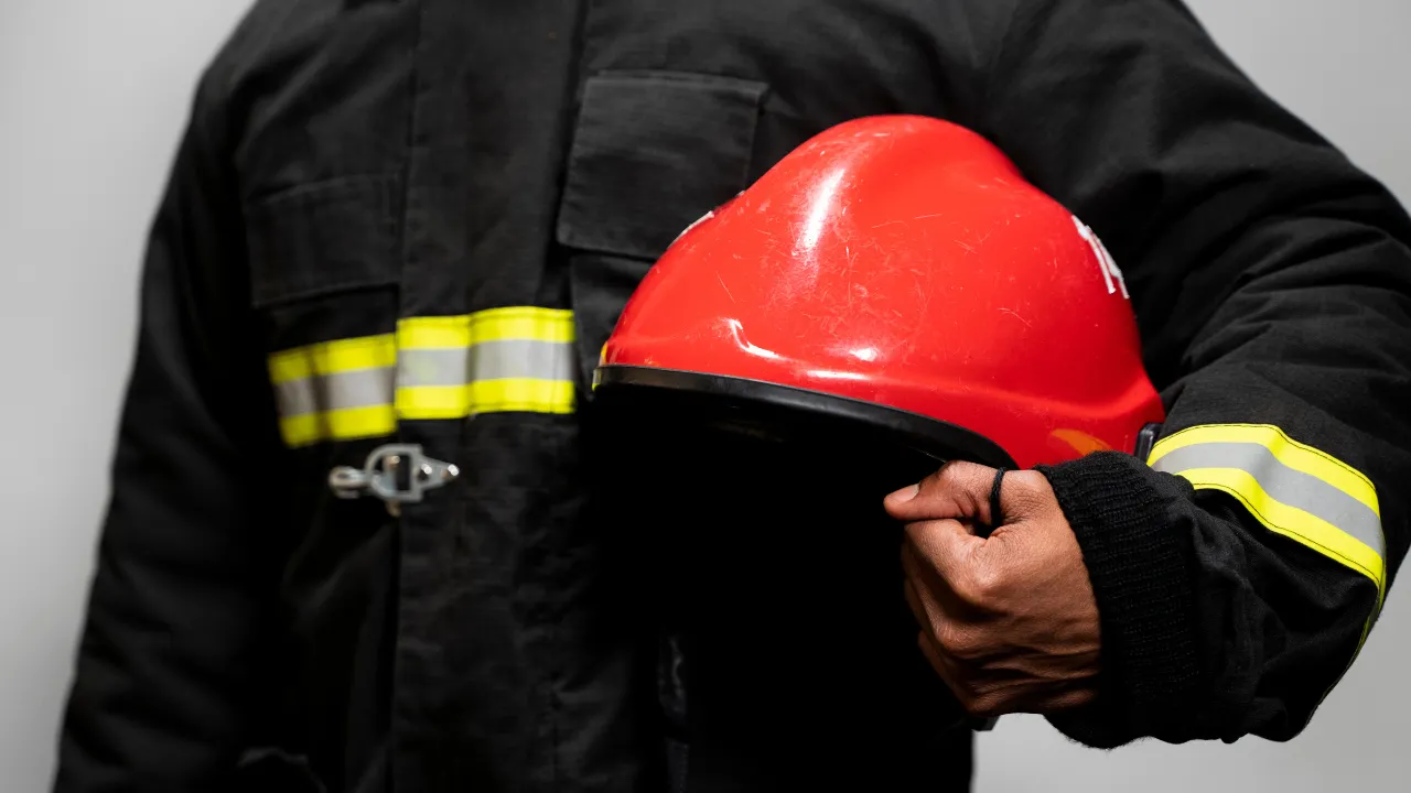 Bombeiro em uniforme com faixas refletivas segurando capacete vermelho, representando conformidade com os Critérios do Corpo de Bombeiros para Aprovação.